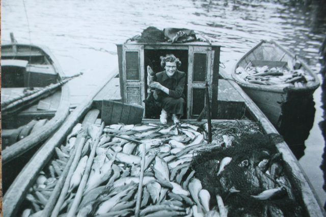 Jack Hann’s skiff&amp;nbsp; "Mary Maureena" with its dory loaded. Mike Fulford’s punt is to the left. The lady is Joan (Furlotte) Walsh weighted down in fish in 1952. Visiting from away, she is overwhelming happy to be on the Island and down around the wharves and boats.